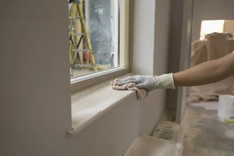 Construction dust being wiped from a windowsill in a freshly renovated room